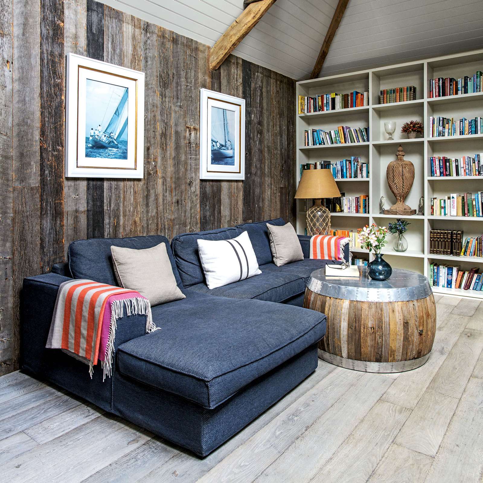 غرفة معيشة ريفية مع جدران مغطاة بألواح خشبية زرقاء على شكل حرف L صوفا وخزائن للكتب
