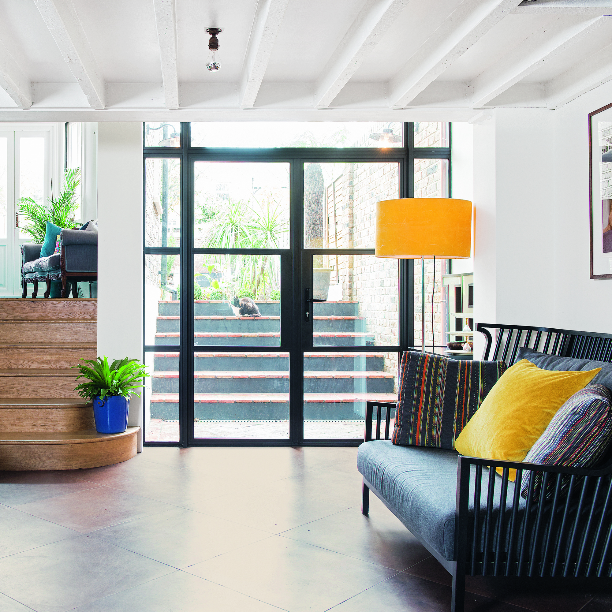 غرفة ببلاط أرضي بني قطري وكرسي مخملي أخضر ومقعد خشبي منجد باللون الرمادي الداكن وباب زجاجي للحديقة.