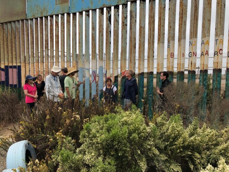 يقف الناس على طول السياج الممتد على الحدود الأمريكية المكسيكية