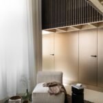 الضوء يتدفق من خلال ستائر مزدوجة الارتفاع تغطي نوافذ الشقق الكبيرة.  جدار أوراق الخشب والبرونز ...