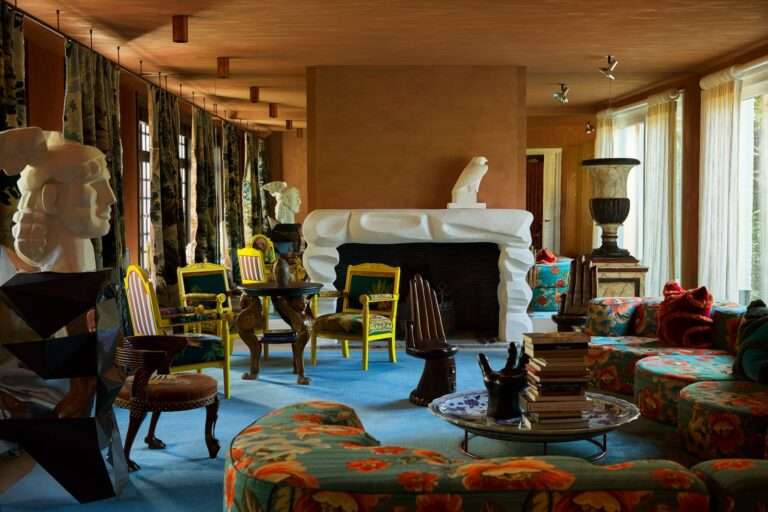 غرفة معيشة مع طاولة طعام صغيرة وأريكة مطبوعة بالزهور ومدفأة بيضاء كبيرة