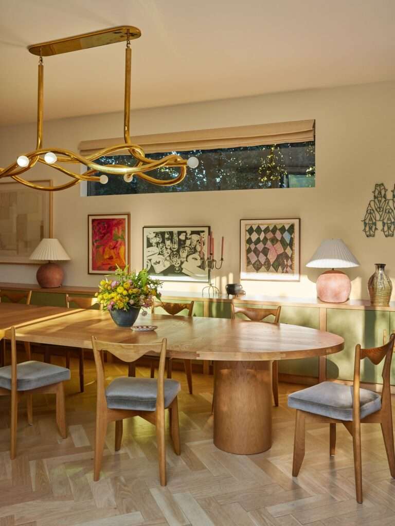 Dining room with long rounded table surrounded by gray upholstered chairs art lining far wall with long rectangular...