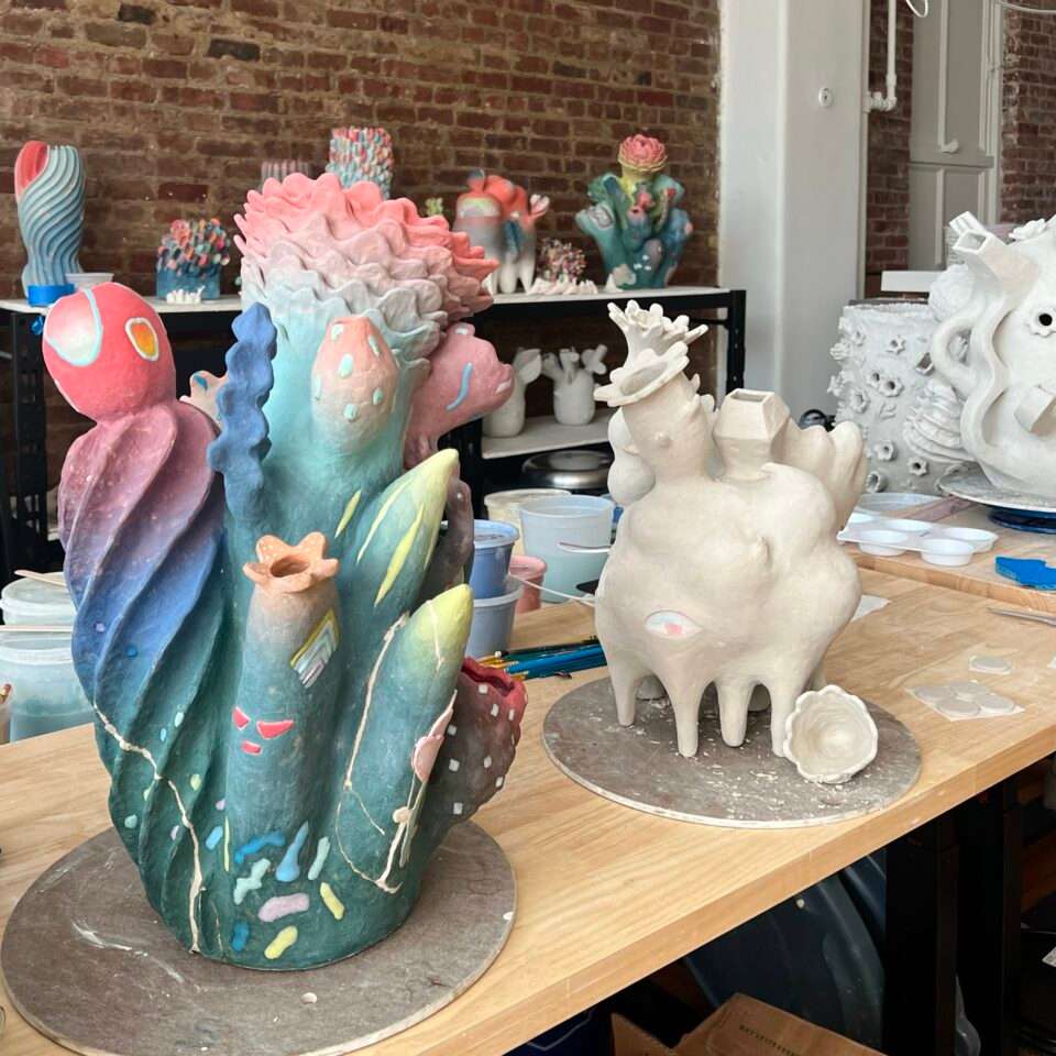a studio view of ceramic sculptures in progress, featuring numerous colors and botanical or coral-inspired shapes