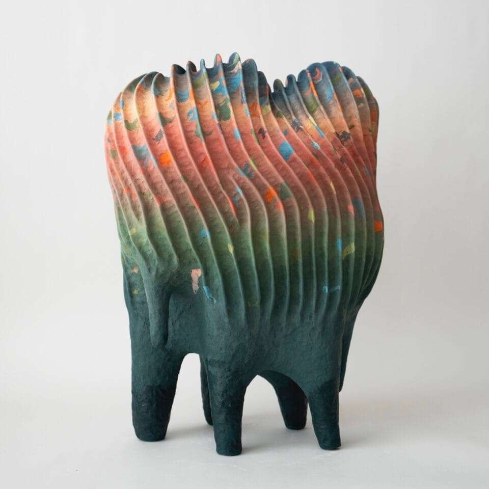an abstract, colorful ceramic sculpture with a linear texture and a color gradient from green to orange to yellow