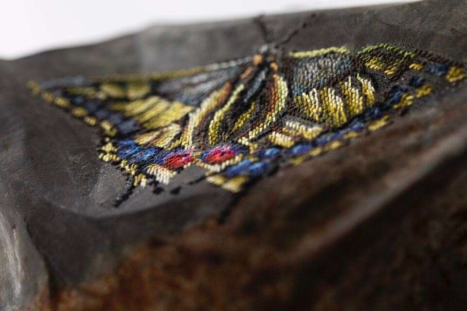 detail of a rusted, round piece of metal with a cross-stitched flower made through perforated holes