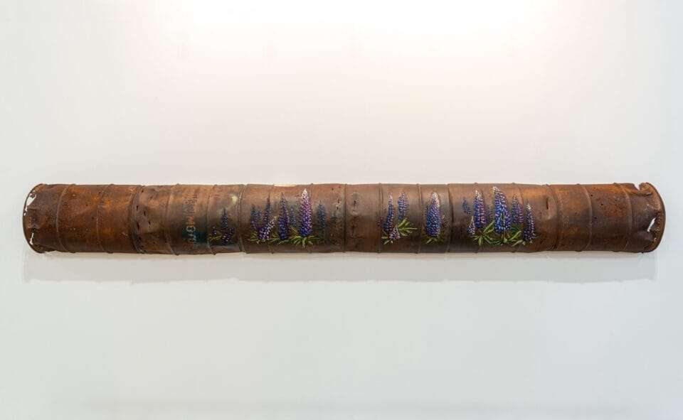 a long, rusted, pipe-like sculpture with cross-stitched flowers along the surface
