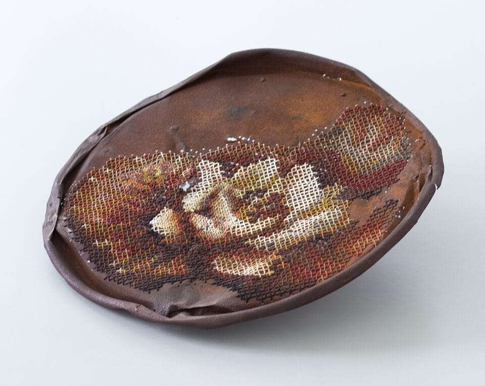 a rusted, round piece of metal with a cross-stitched flower made through perforated holes