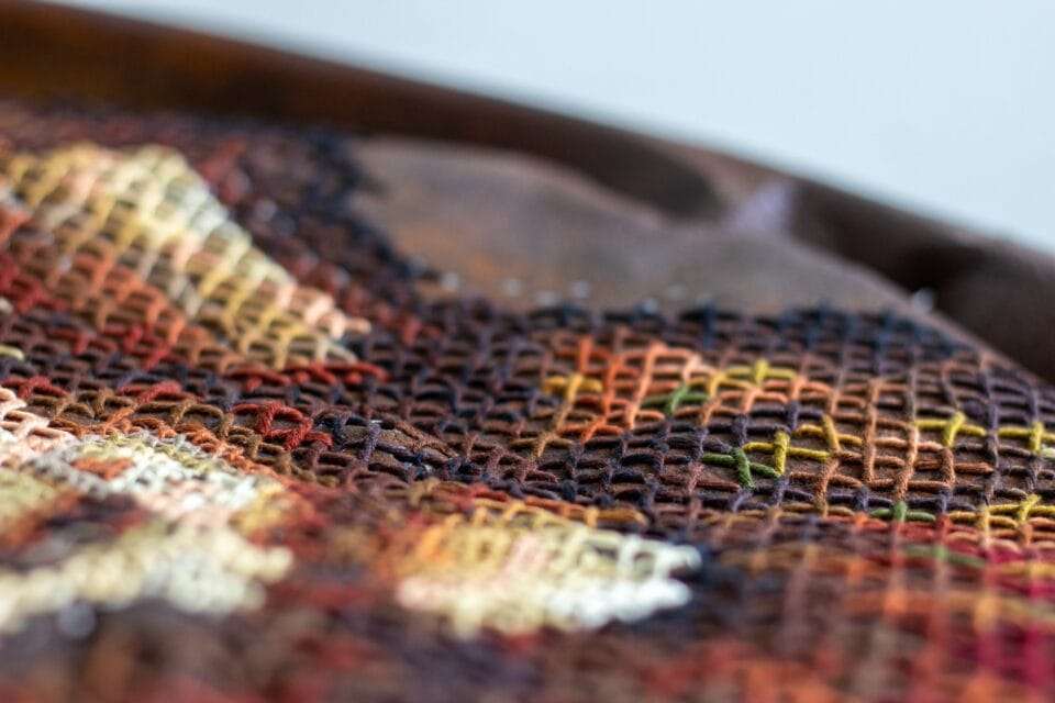 a detail of a rusted, round piece of metal with a cross-stitched flower made through perforated holes