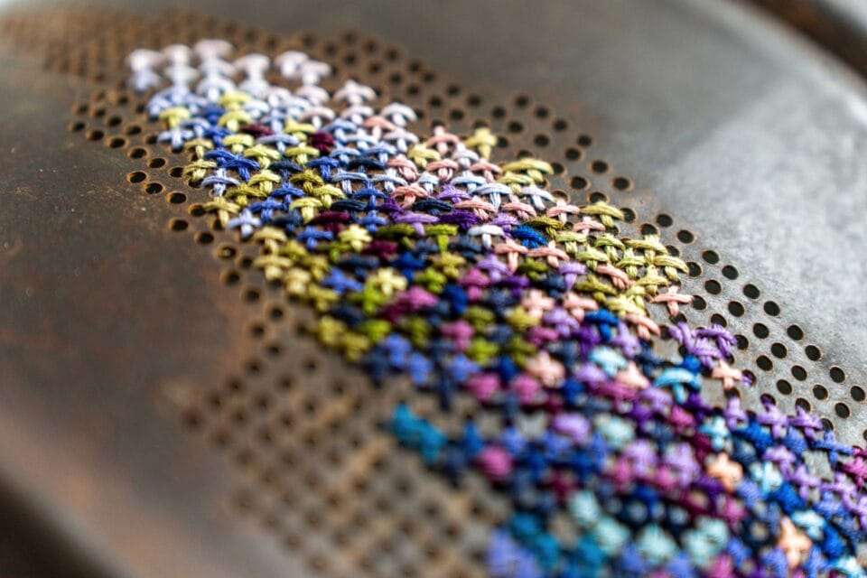a detail of a cross-stitched flower in a rusted piece of metal