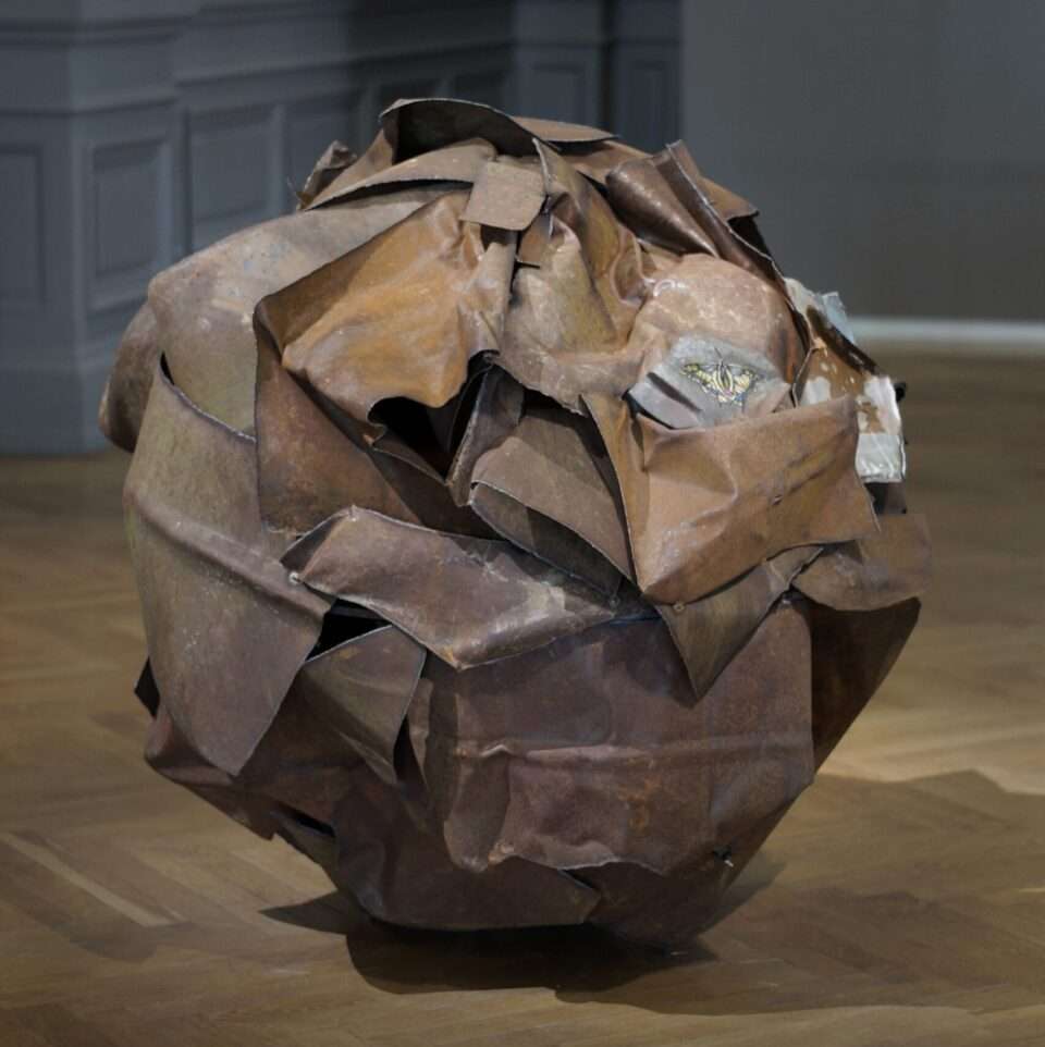 a large rusted ball of metal with a cross-stitched butterfly in one area