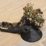 two bronze figures lay on the floor with flowers growing from them