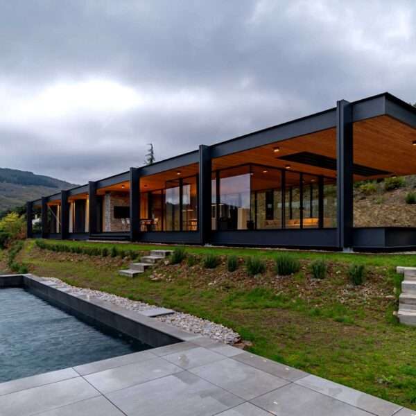 A modern house with a horizontal layout, walls of glass, and an exposed steel structure.