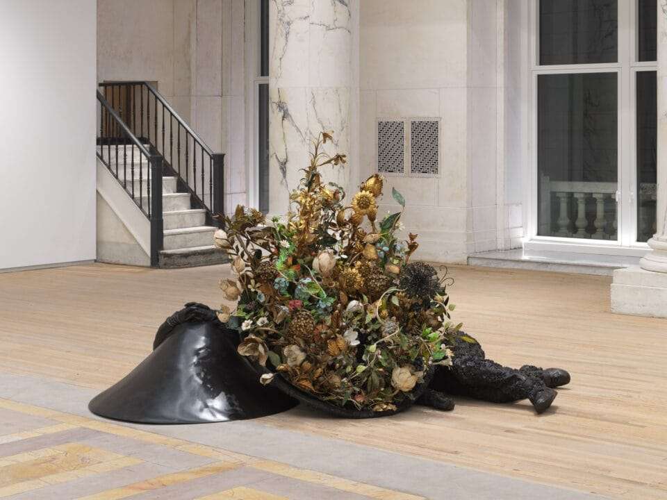 two bronze figures lay on the floor with flowers growing from them