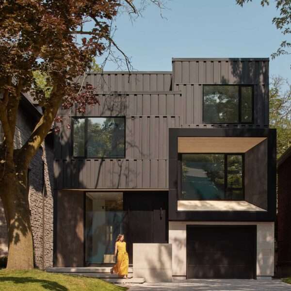 The exterior of this modern home is composed of a series of interlocking volumes, with the upper storeys set back to provide a gentle transition from street level. Clad in rhythmically patterned black metal, the facade is accentuated by warm wood siding and porcelain slabs.