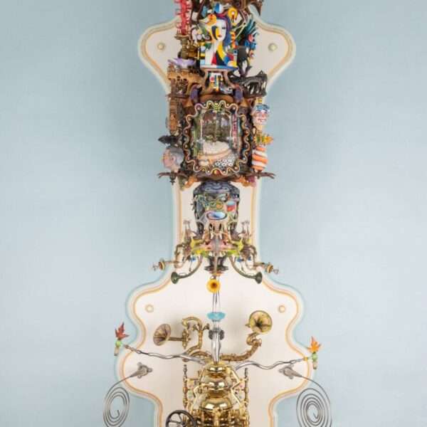 an elaborately detailed sculpture with numerous sculpted, found, and painted elements installed on an ornately shaped white panel, with some of the elements able to be moved and rotated to show different scenes