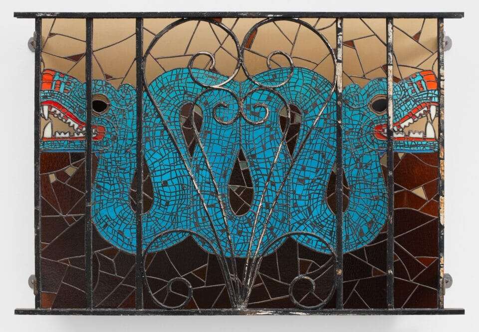 a wall sculpture of stained glass depicting a blue serpent, installed behind a fence