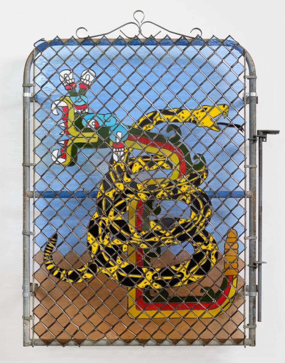 a wall sculpture of stained glass depicting a coiled yellow snake on a blue background, installed behind a chainlink gate