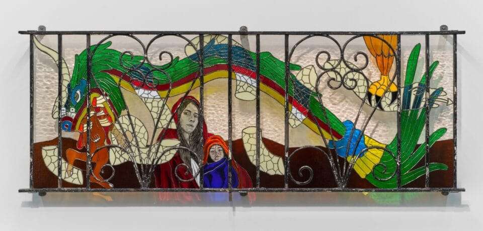 a wall sculpture of stained glass depicting a green dragon alongside a portrait of a mother and child, installed behind a fence