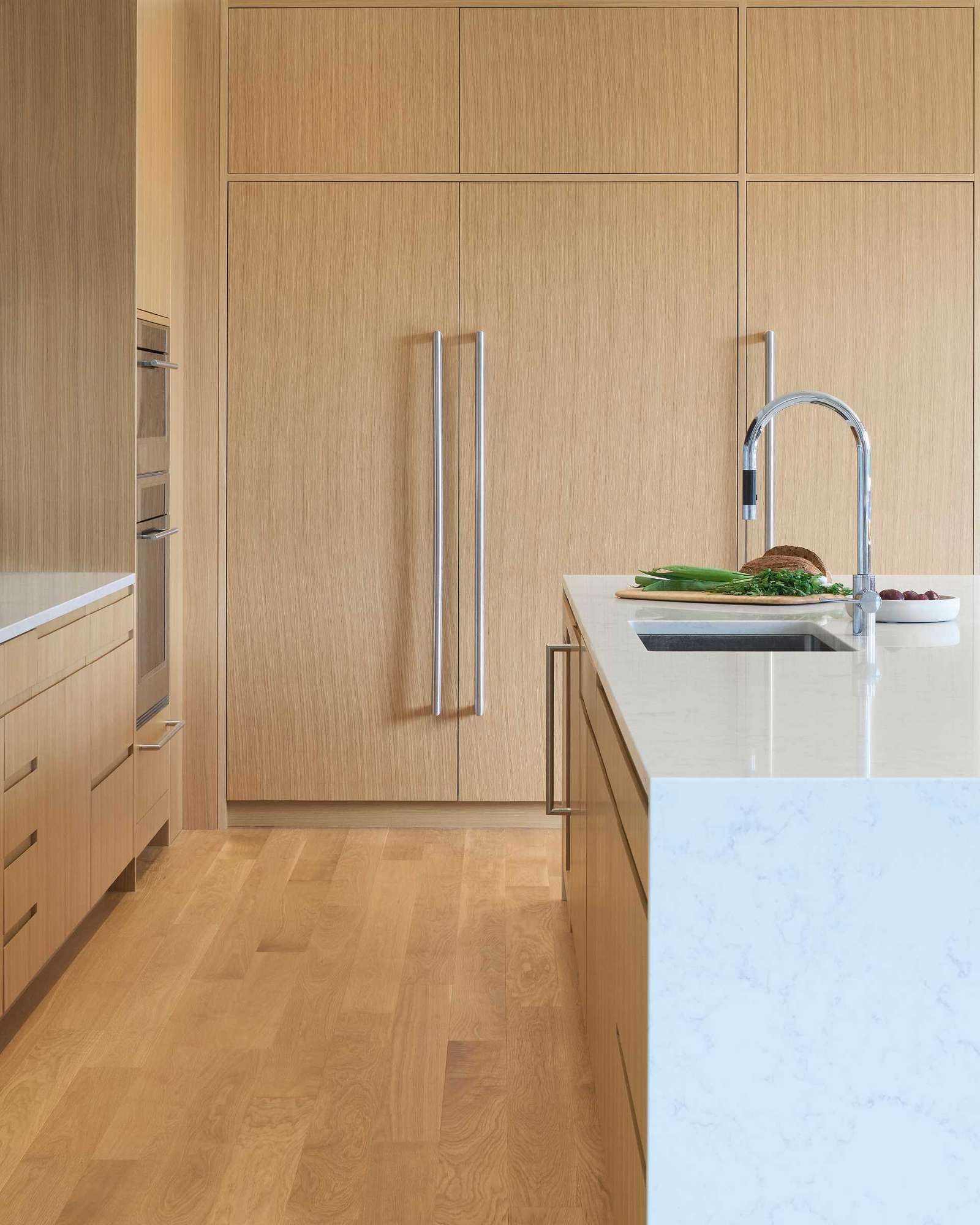 A wood kitchen has integrated appliances and a large island. Nearby there's a casual banquette dining area and the open plan dining room.