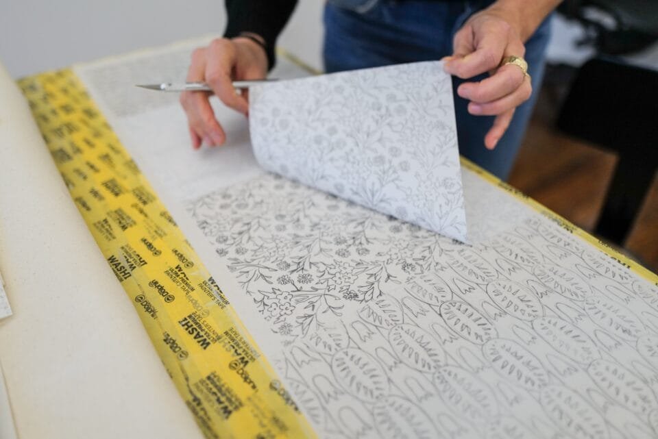 an artwork in progress in Ruby Sky Stiler's studio, showing a transfer stencil of a pattern onto canvas that she is slowly peeling back
