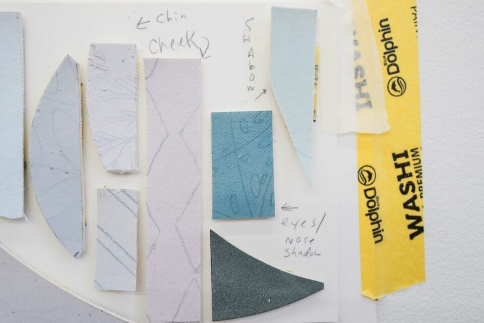 pieces of canvas and yellow tape pasted on a surface with notes about the placement on a painting, like "cheek" and "chin" marked in pencil