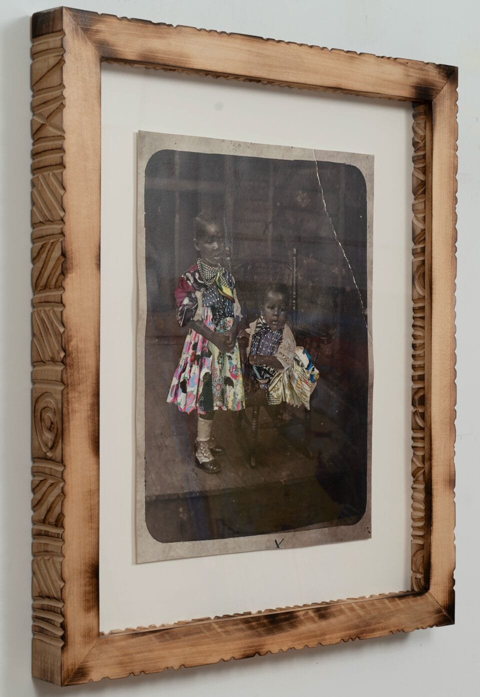 a side view of a collage of black and white photos and colorful textiles in a carved wooden frame. the photo depicts two small children