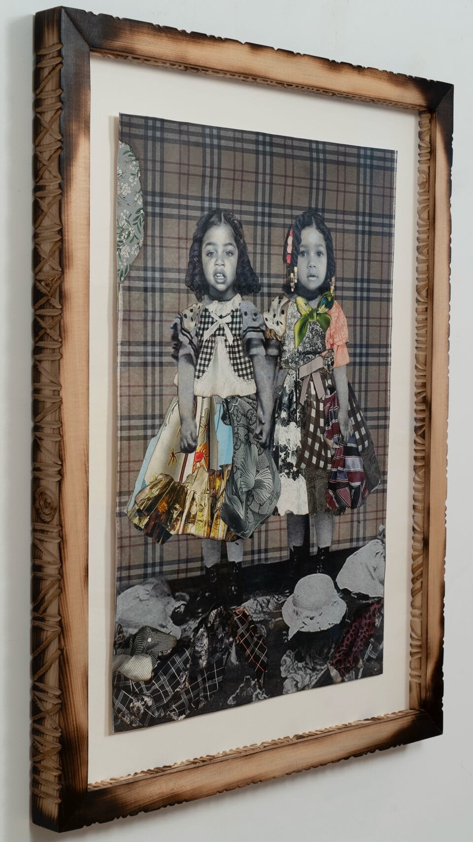 a collage of black and white photos and colorful textiles in a carved wooden frame. the photo depicts two little girls