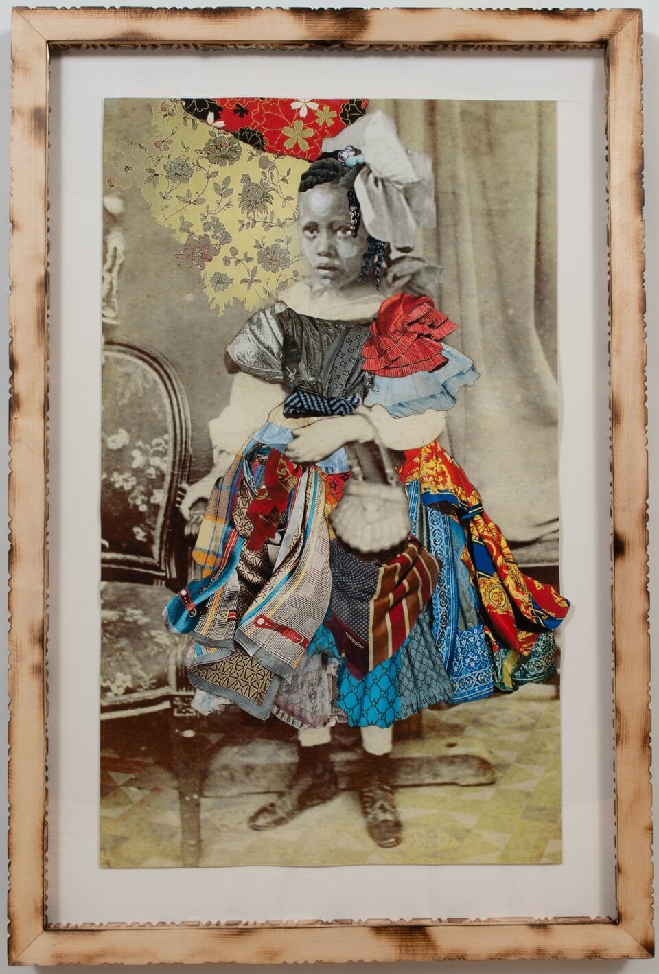 a collage of black and white photos and colorful textiles in a carved wooden frame. the photo depicts a little girl