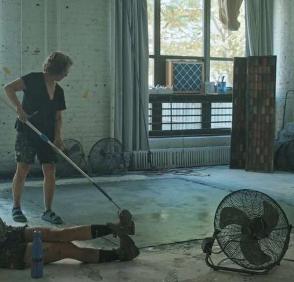 a younger woman sits on the floor while an older woman paints a canvas with a roller