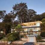 A modern waterfront home features a lightweight floating roof and timber stacking doors that slide away to open the living areas completely to the external terraces and verandah.