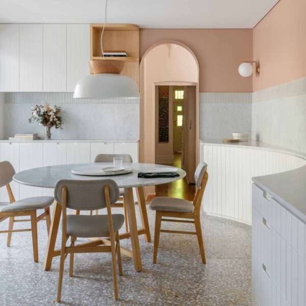 In this modern dining area, earthy peach painted above the tile datum helps to centre and hold the space, while a circular Jardan marble dining table is central to the space, and a curved timber panelled joinery lines the wall.