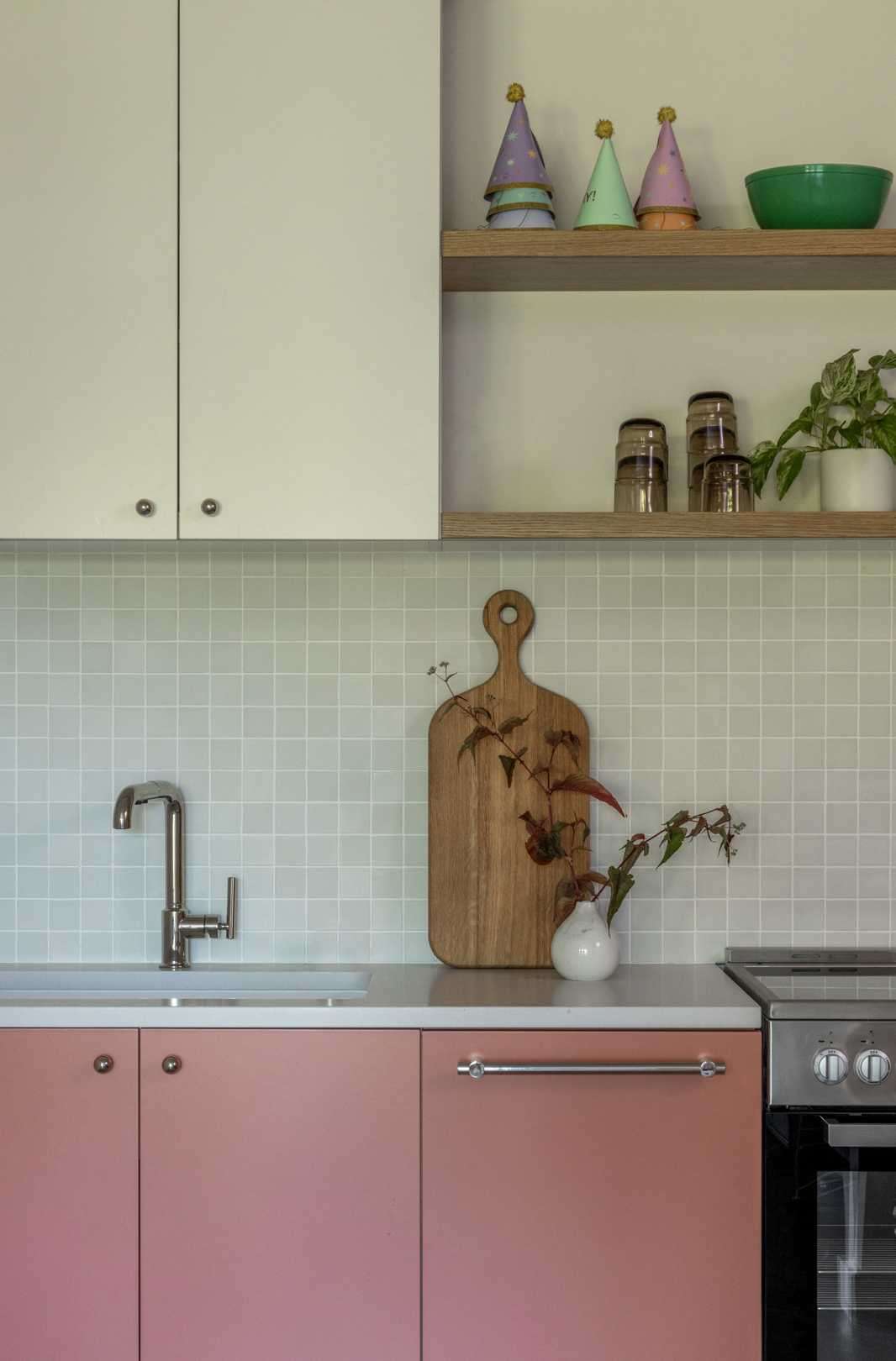 A kitchenette with tile backsplash and blush pink lower cabinets.