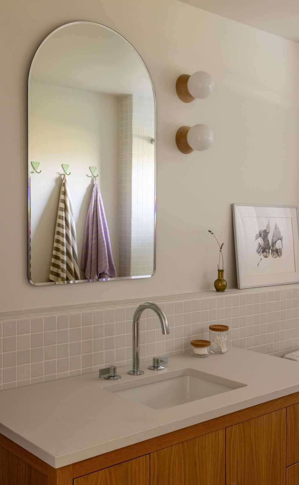 A contemporary bathroom with square tiles and an arched mirror.