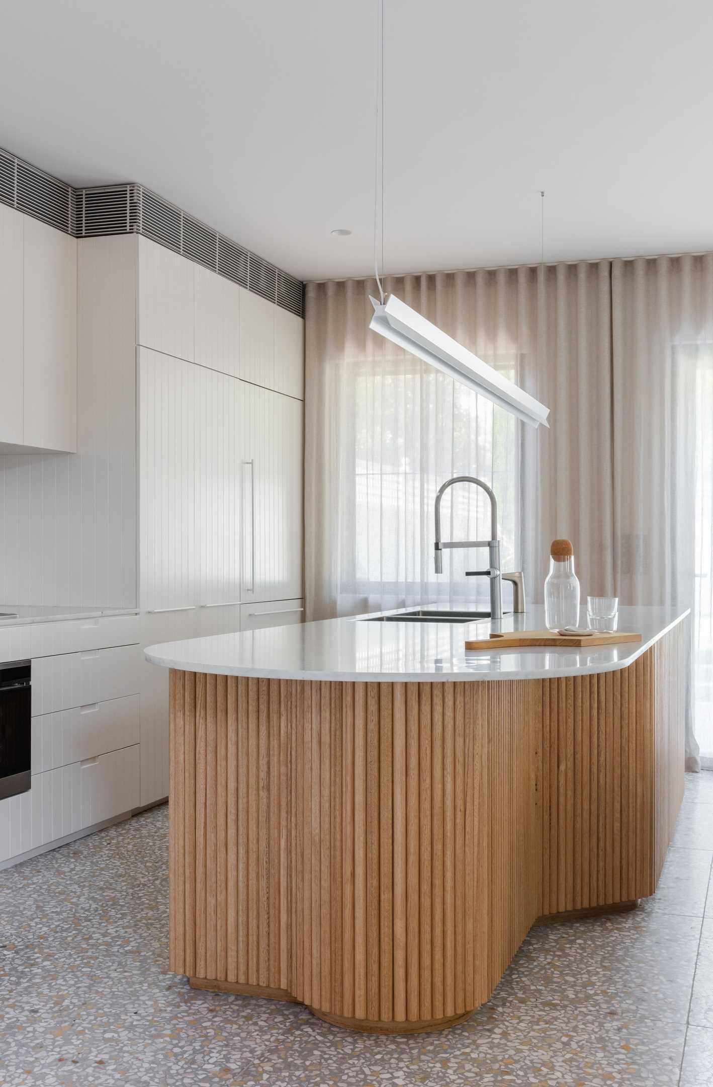 In this modern kitchen, the island features a hand-crafted with a scalloped timber base, topped with marble, holding court like those that sit around the island might.
