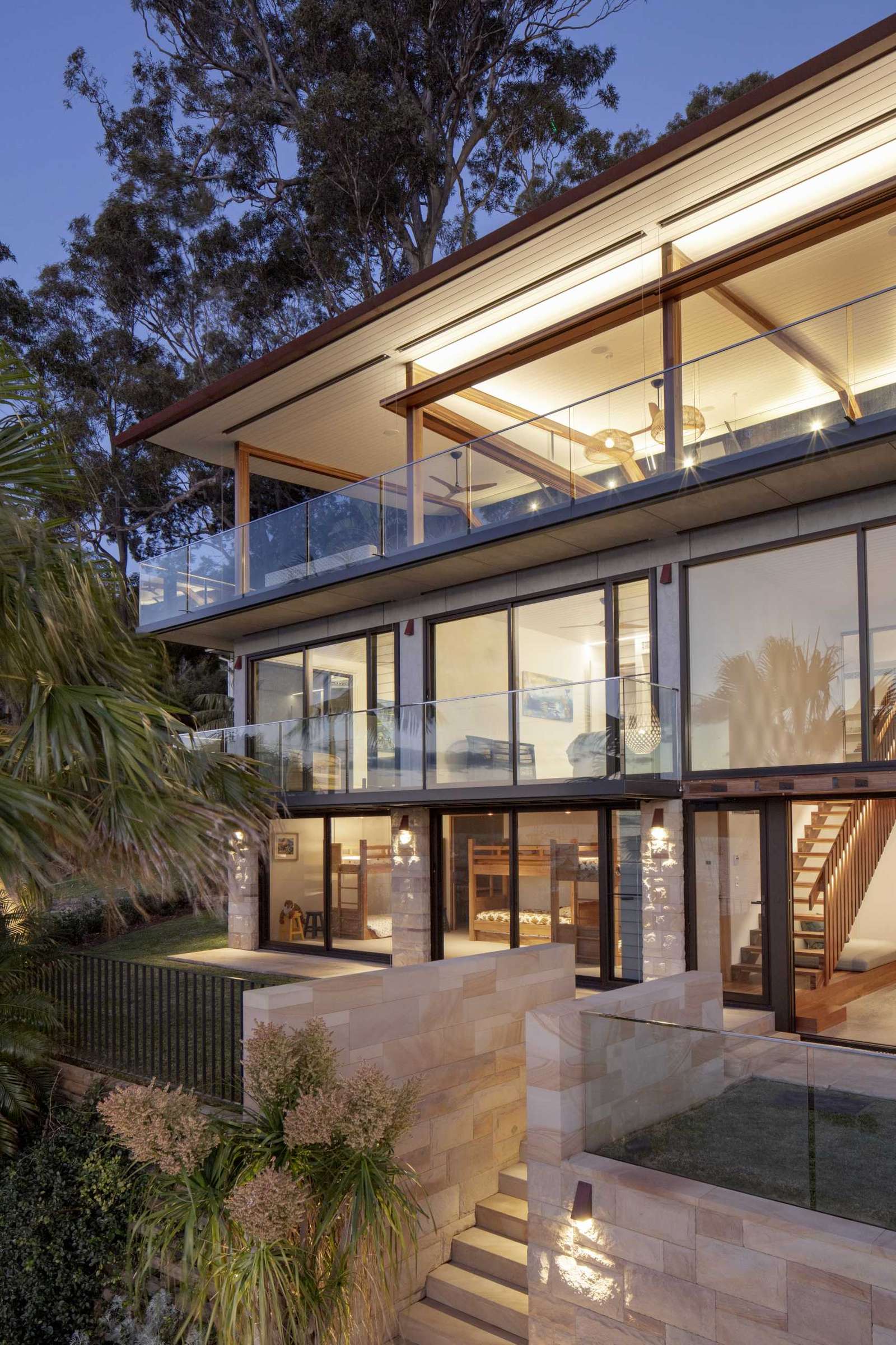 A modern waterfront home features a lightweight floating roof and timber stacking doors that slide away to open the living areas completely to the external terraces and verandah.