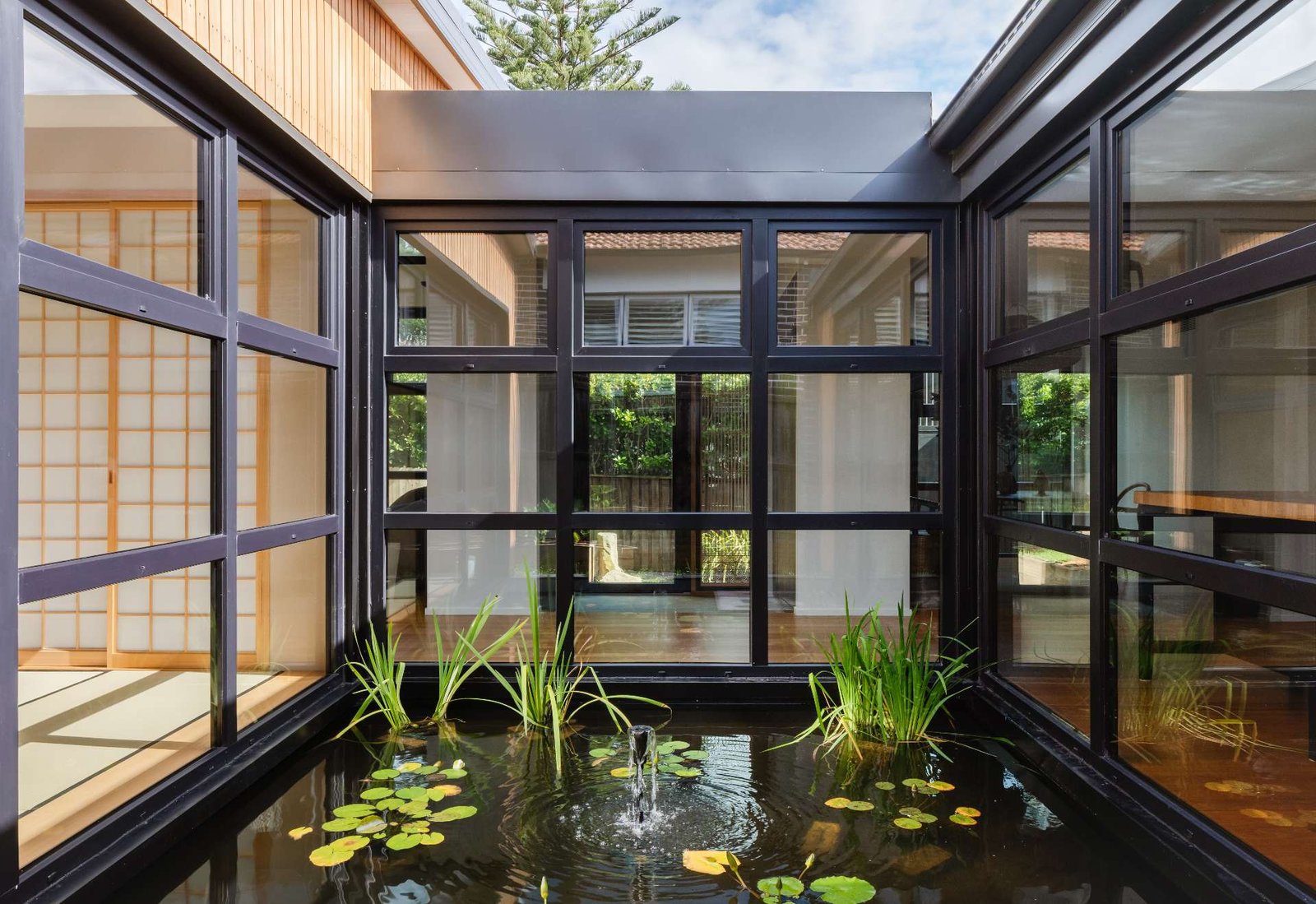 A tranquil courtyard reflection pond forms the serene heart of this home, framed by  black steel windows that invite nature into every room.
