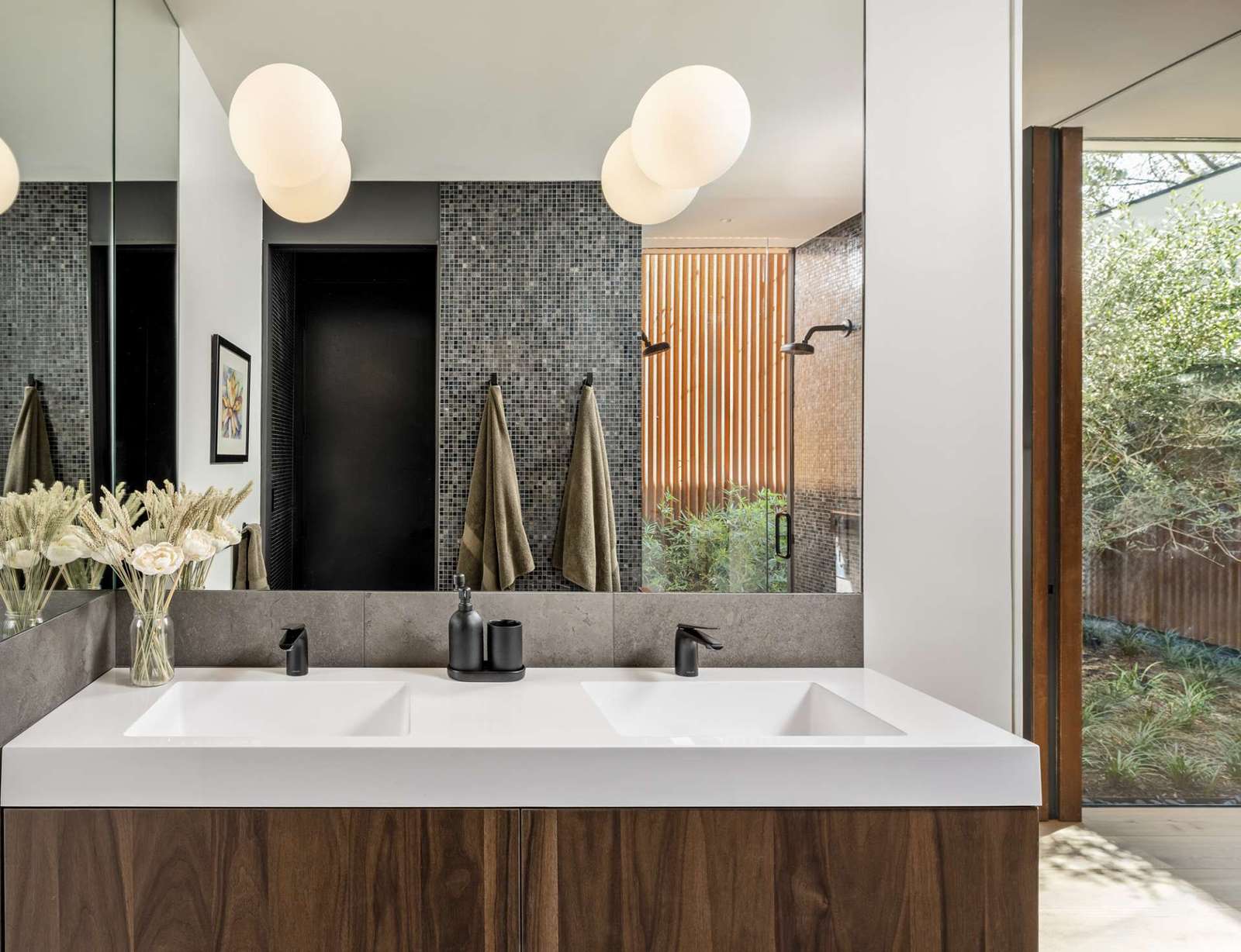 Clean lines and earthy textures define this spa-like bathroom. The floating walnut vanity and matte black fixtures feel warm yet modern, while a glass shower opens to a private garden framed by vertical cedar slats.