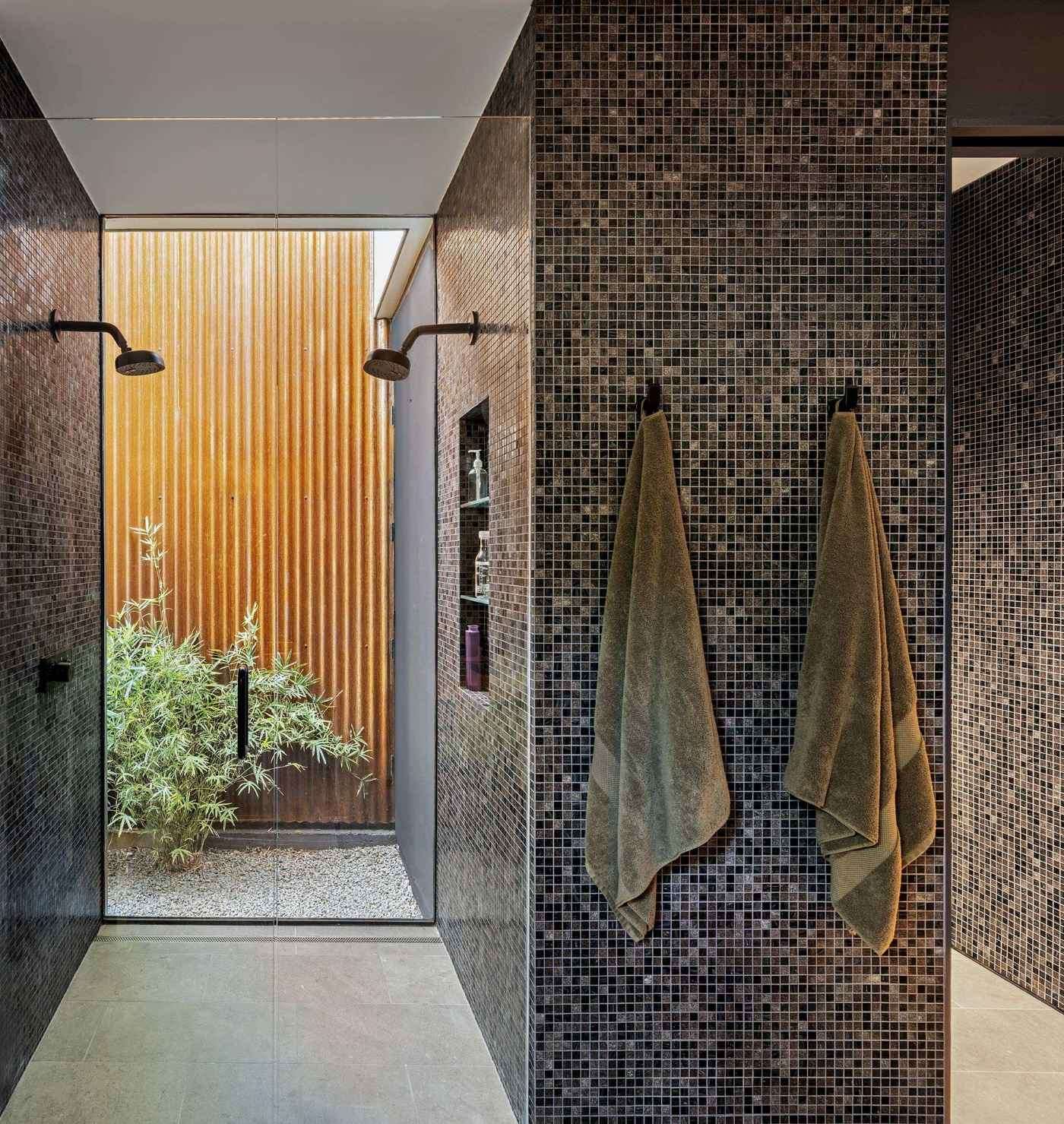This moody double shower pairs rich mosaic tile with a glass wall that opens to a minimalist courtyard. The balance of dark texture and natural light gives the space a grounded, spa-like feel.