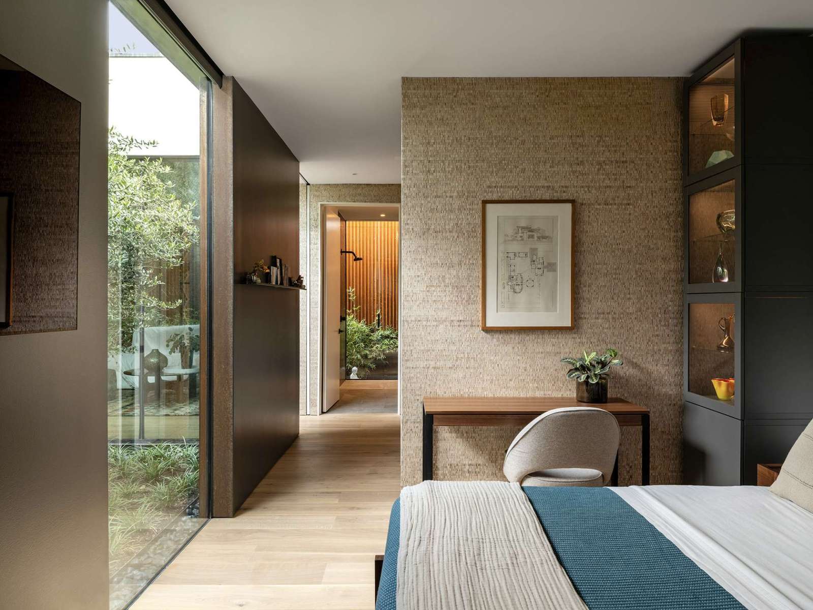 This serene bedroom blends soft textures with sleek lines, opening to a tranquil courtyard garden. Floor-to-ceiling glass draws nature inward, while warm wood floors and grasscloth walls ground the space in quiet luxury.