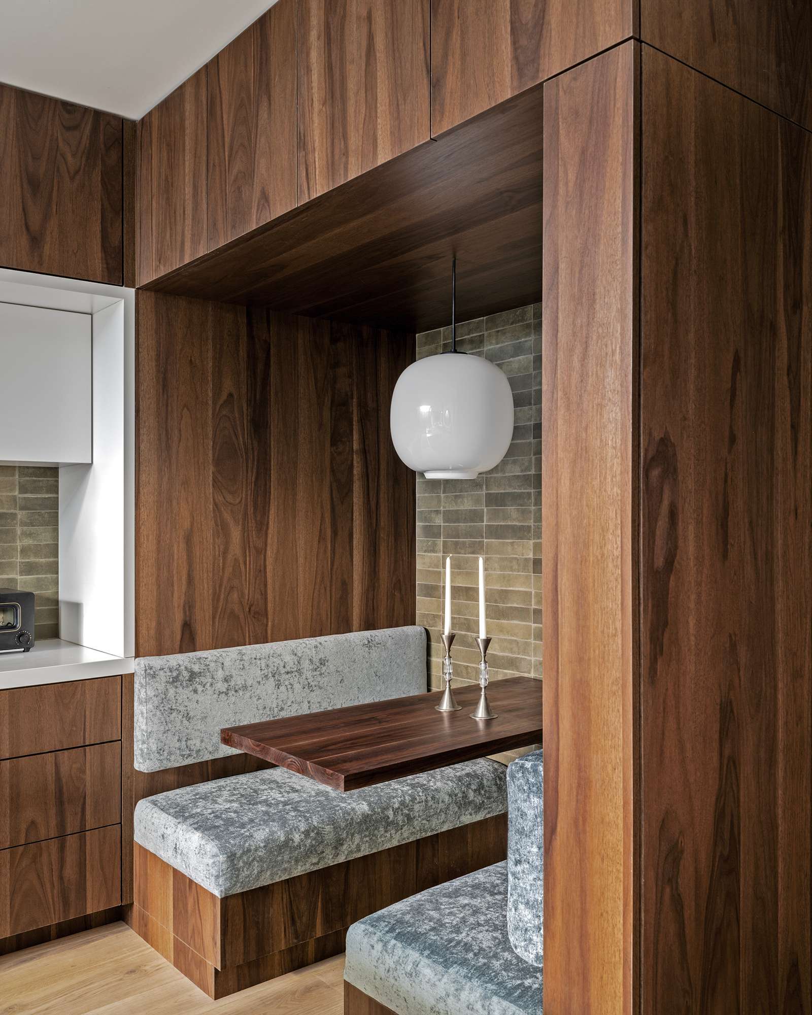 Rich wood cabinetry sets a warm tone in this modern kitchen, where clean white countertops and olive-toned backsplash tiles add depth. A built-in breakfast nook doubles as a cozy workspace, blending form and function beautifully.