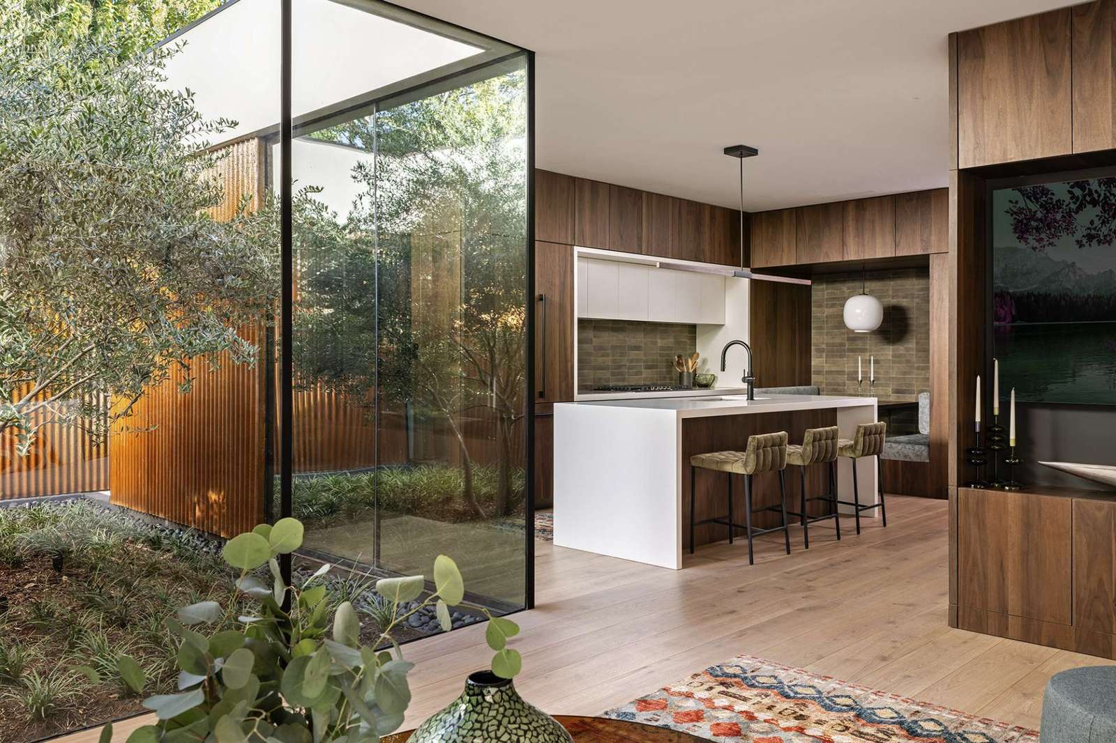 Rich wood cabinetry sets a warm tone in this modern kitchen, where clean white countertops and olive-toned backsplash tiles add depth. A built-in breakfast nook doubles as a cozy workspace, blending form and function beautifully.