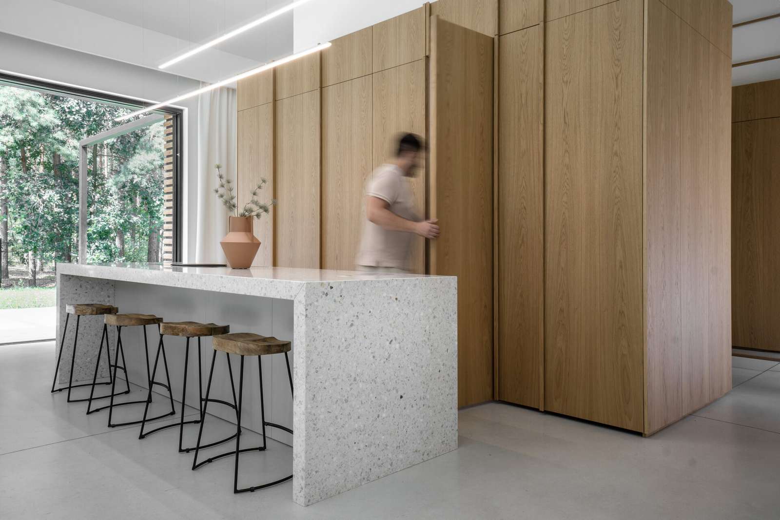In this modern kitchen, the island stands out as a centerpiece, crafted from terrazzo, which adds a unique texture and visual interest, while the wood cabinetry hides the sink and the fridge.