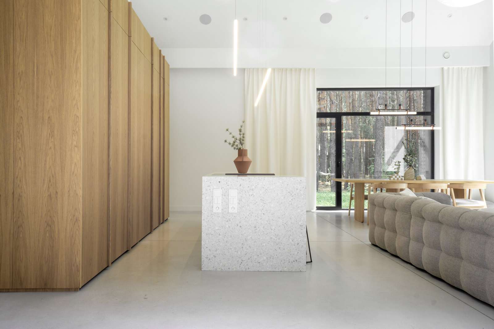 In this modern kitchen, the island stands out as a centerpiece, crafted from terrazzo, which adds a unique texture and visual interest, while the wood cabinetry hides the sink and the fridge.