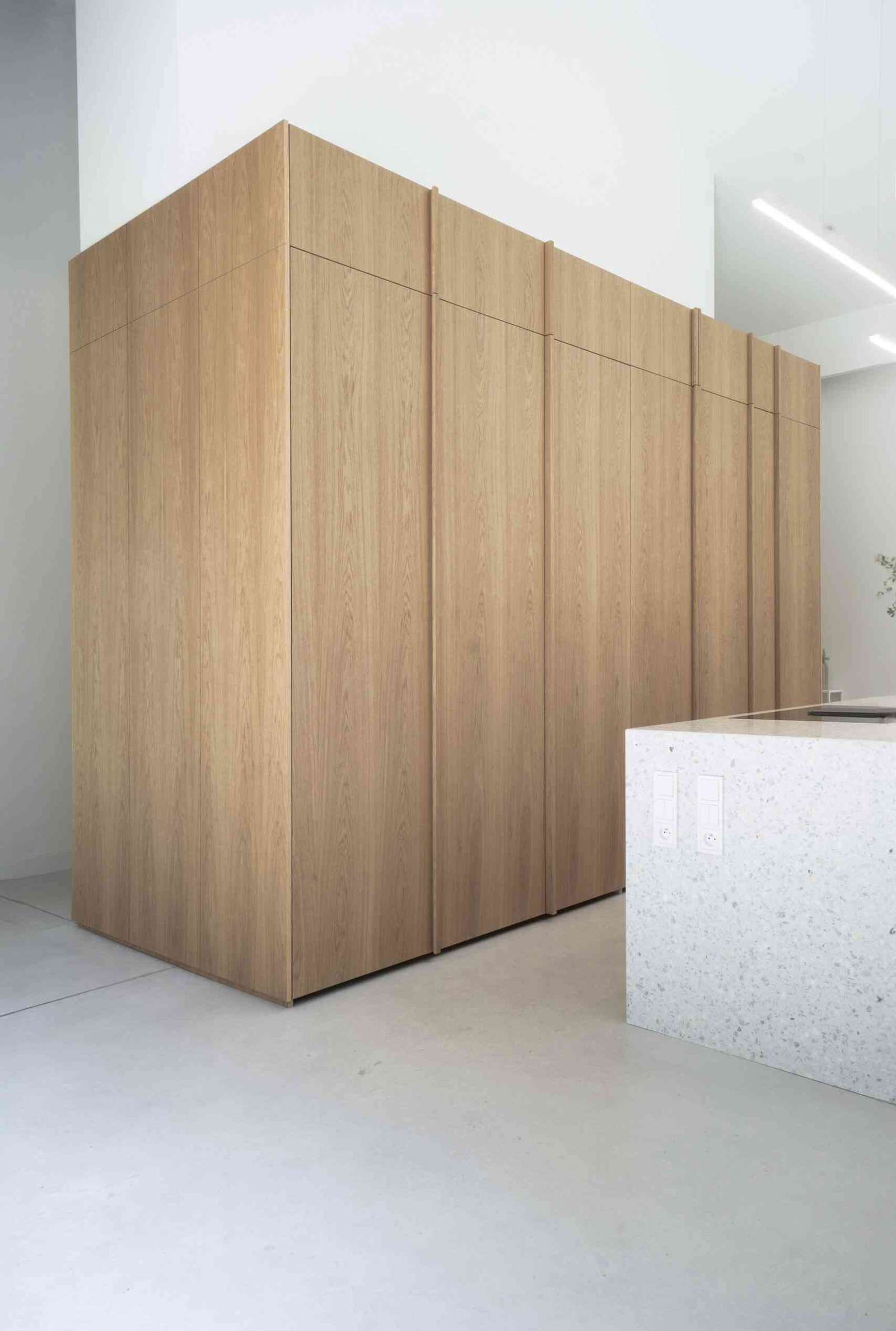 In this modern kitchen, the island stands out as a centerpiece, crafted from terrazzo, which adds a unique texture and visual interest, while the wood cabinetry hides the sink and the fridge.