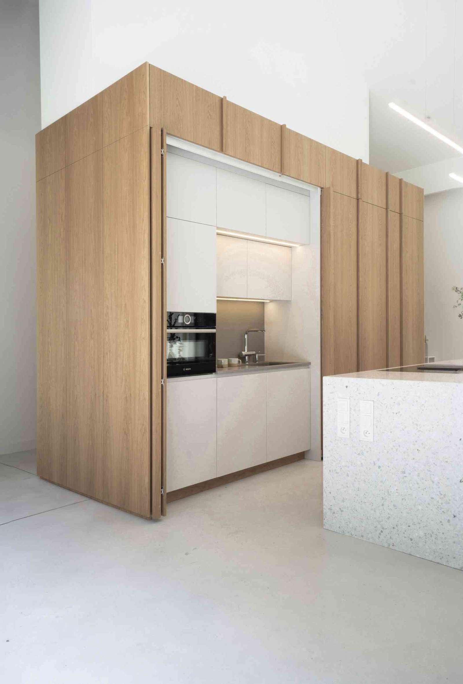 In this modern kitchen, the island stands out as a centerpiece, crafted from terrazzo, which adds a unique texture and visual interest, while the wood cabinetry hides the sink and the fridge.