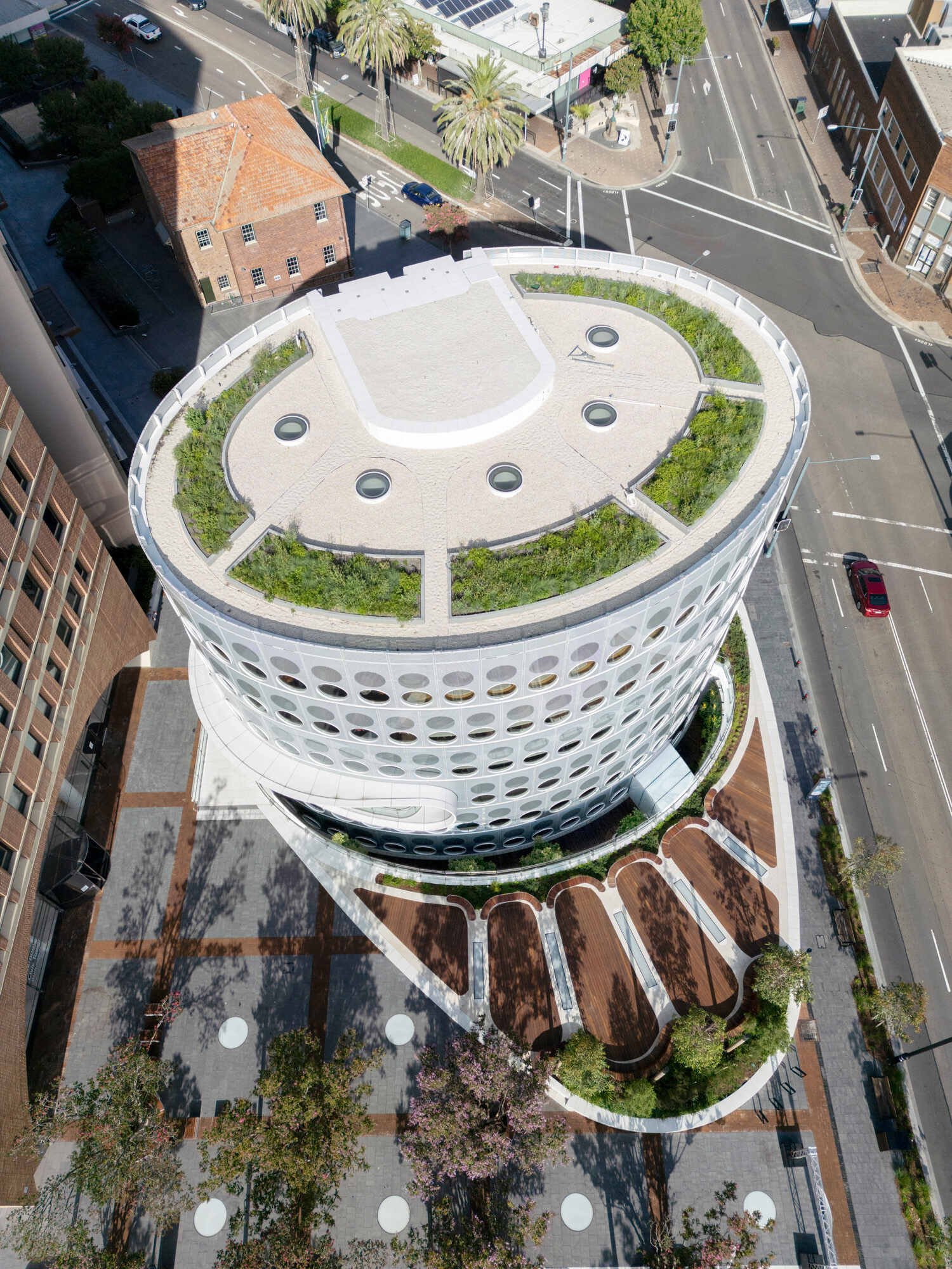 A modern library with a round design and green roof, whose exterior facade is covered in matching round windows.