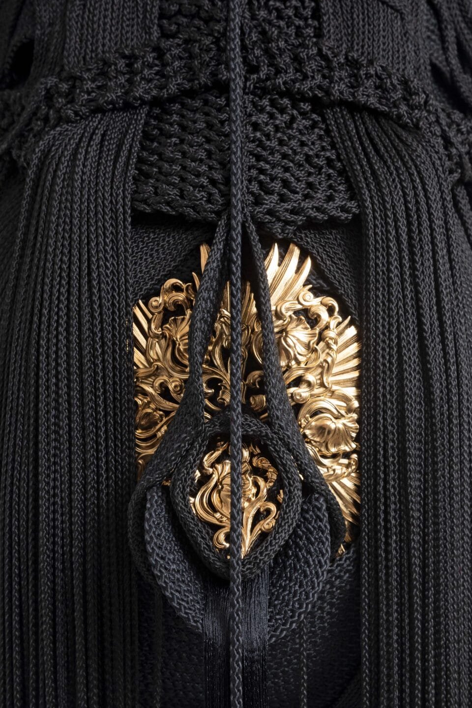 a detail of a sculpture made from black cord, thread, and metal