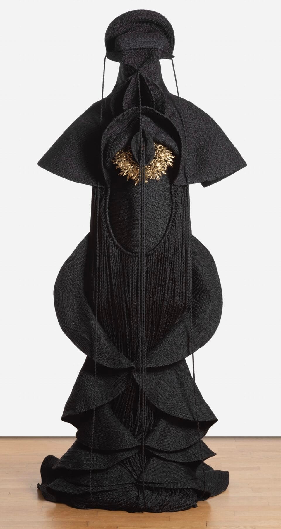 a sculpture made from black cord, thread, and metal in the form of a figure or long, dramatic garment