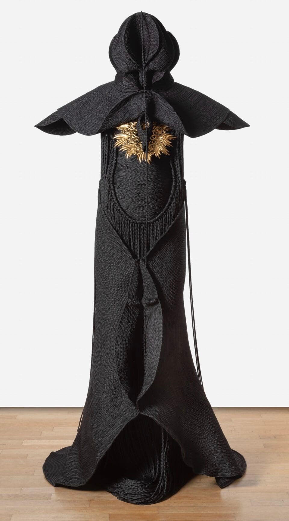 a sculpture made from black cord, thread, and metal in the form of a figure or long, dramatic garment