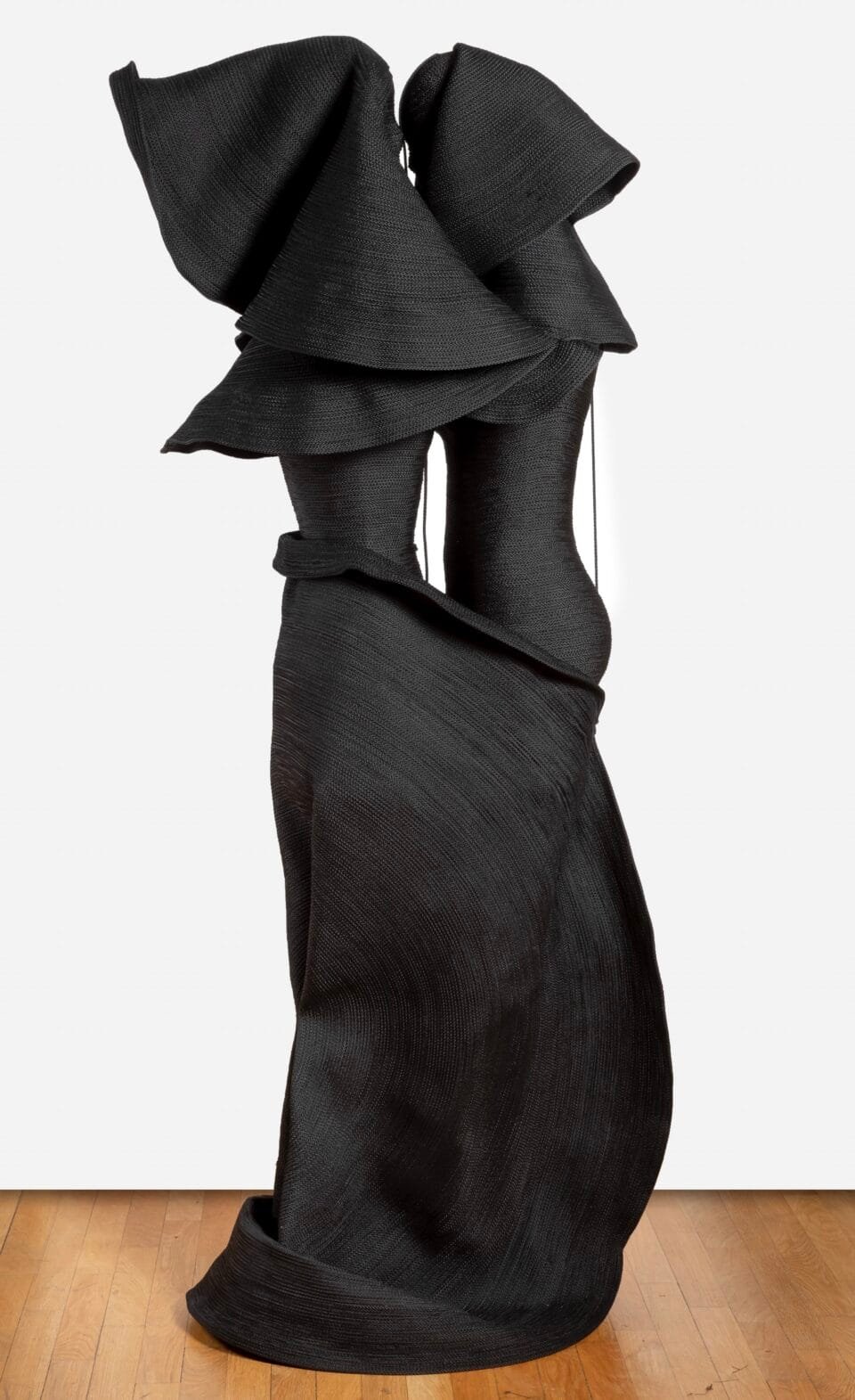 a sculpture made from black cord, thread, and metal in the form of two conjoined figures or a long, dramatic garment